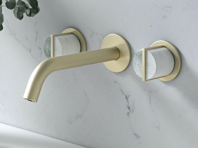 Close up of wall mounted brass basin taps with central spout and two handles