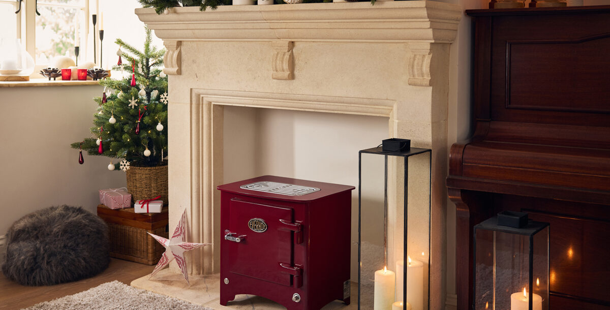 A red stove in a fireplace decorated for Christmas