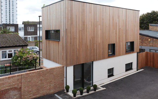 Exterior of a rectangular house built to Passivhaus standard. The top have is timber clad with white render below