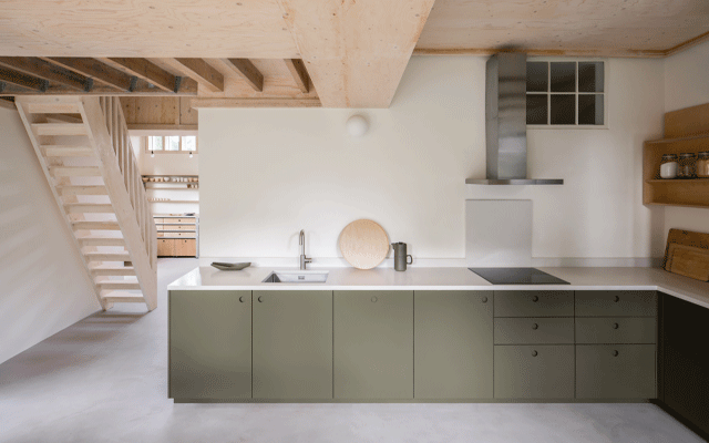 L-shape kitchen layout in open-plan space with green base cabinets and white worktop