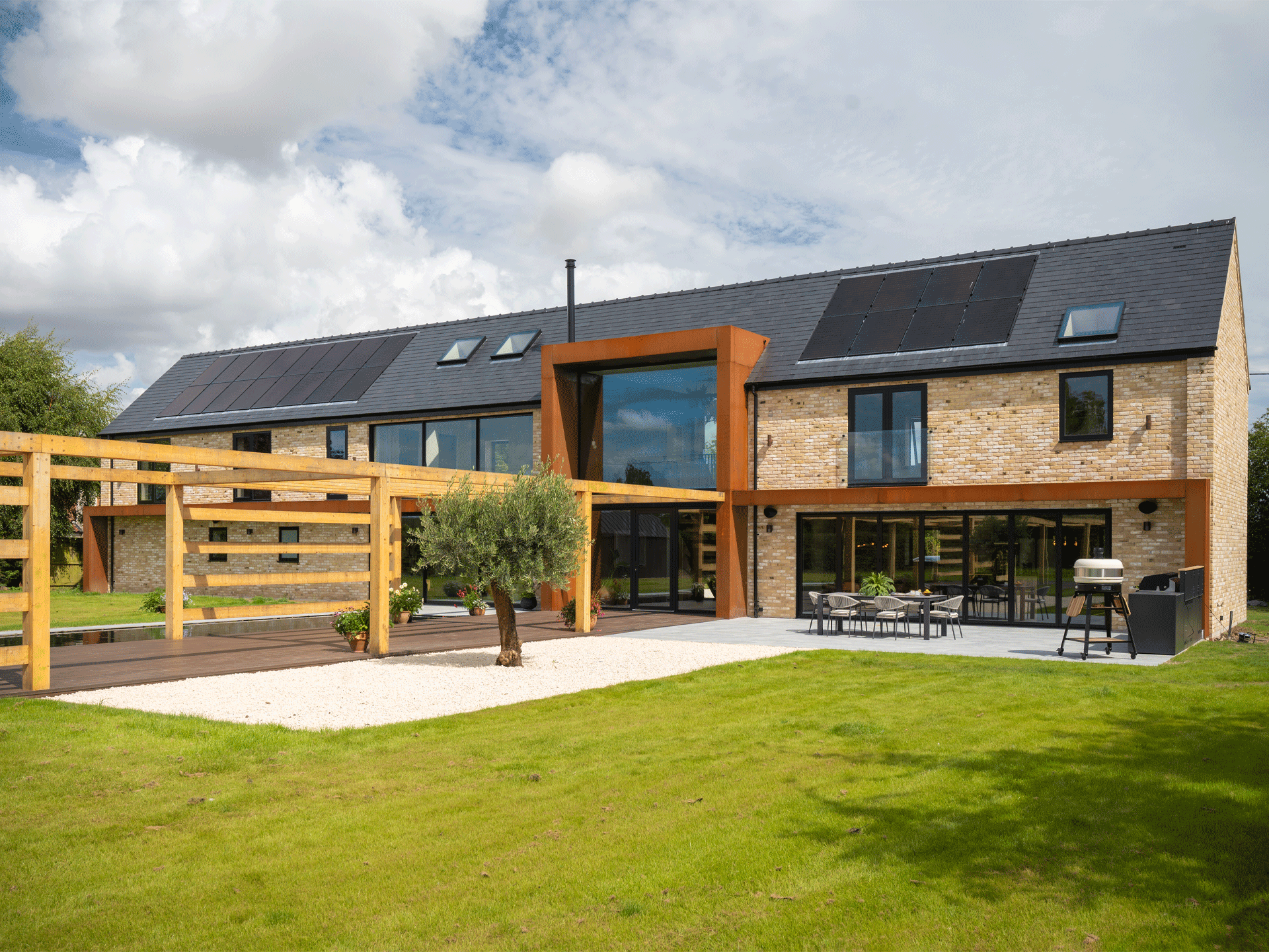 The rear exterior of a self-build brick and corten steel house with a timber pergola